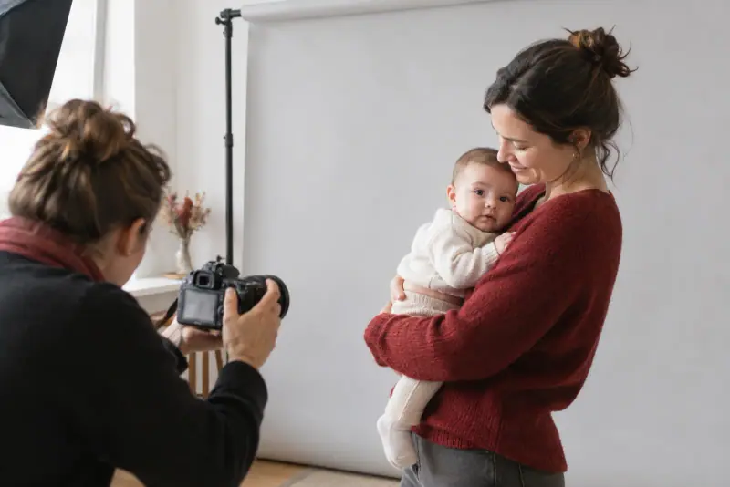 Un photographe prépare une photo d'identité de bébé devant un fond clair dans un studio sobre et bien éclairé.